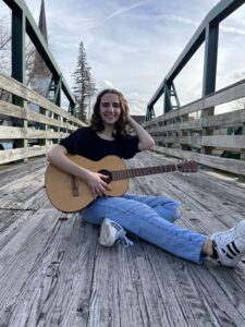 Student poet Hannah Camiolo sitting on bridge with guitar