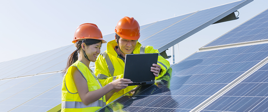 Man and woman reviewing a laptop screen next to a set of industrial-scale solar panels.