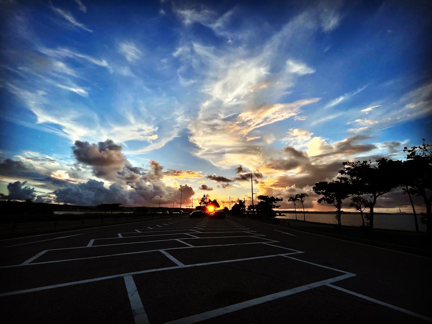 Photo of blue sky with clouds and parking lot in lower darker part of photo