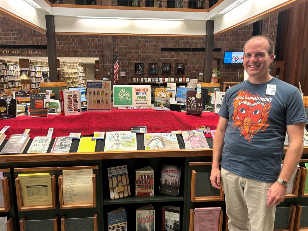Banned book display in background with Part Time Reference Librarian Bryan Schuff in foreground wearing his Read Banned Books t-shirt