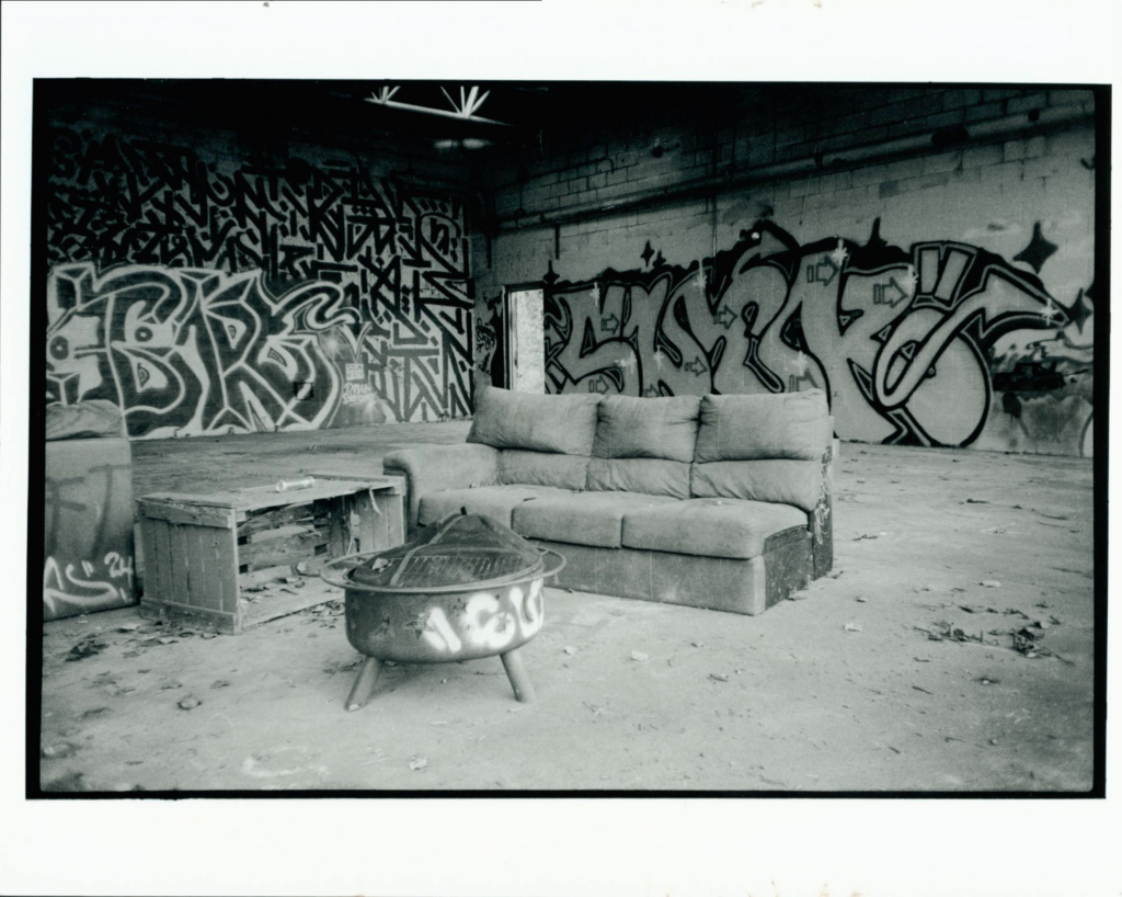 black and white image of abandoned building with graffiti and furniture occupying the space