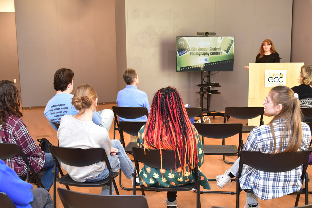 photo of the backs of audience members at the awards ceremony with a presentation screen and woman standing at podium