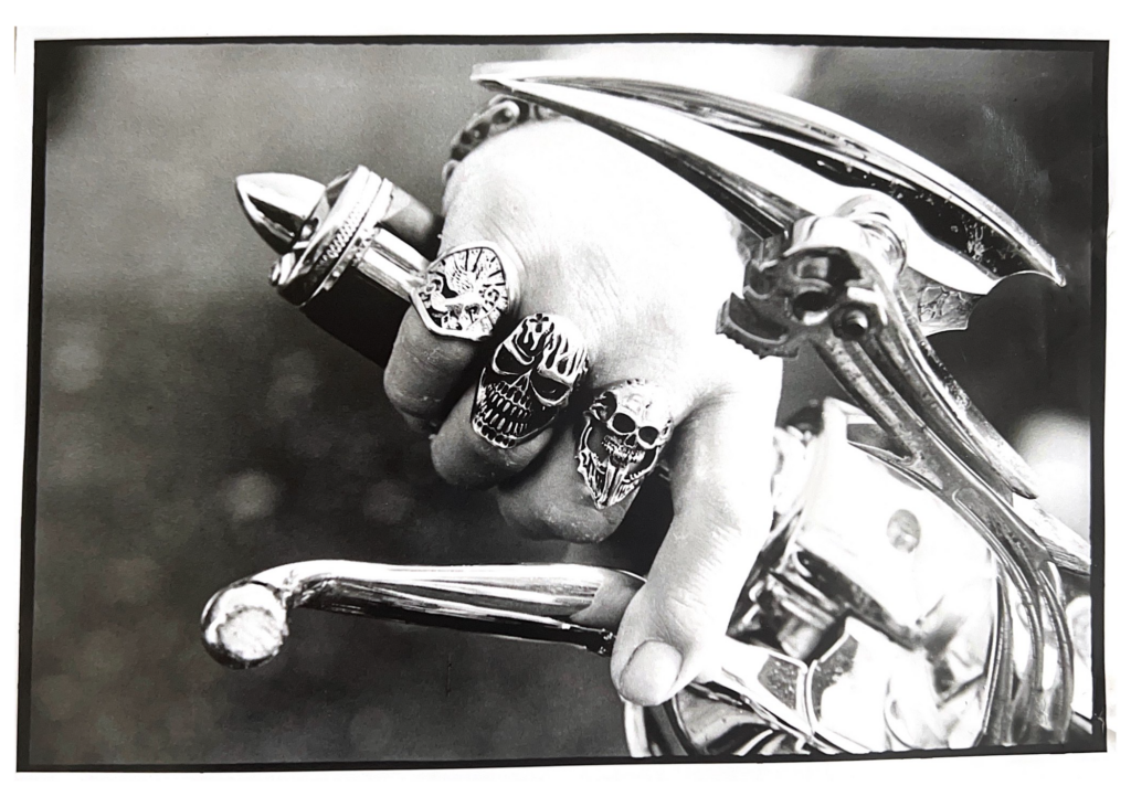 Black and white photo of hand on motorcycle handles with skull rings