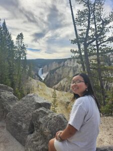 Young woman sitting on rocks with trees, sky, and mountainous ridges and valleys in the background