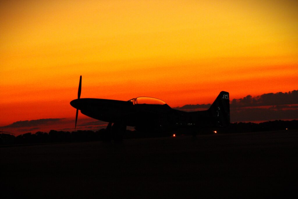 Small airplane sitting on ground with orange and yellow sunset in background