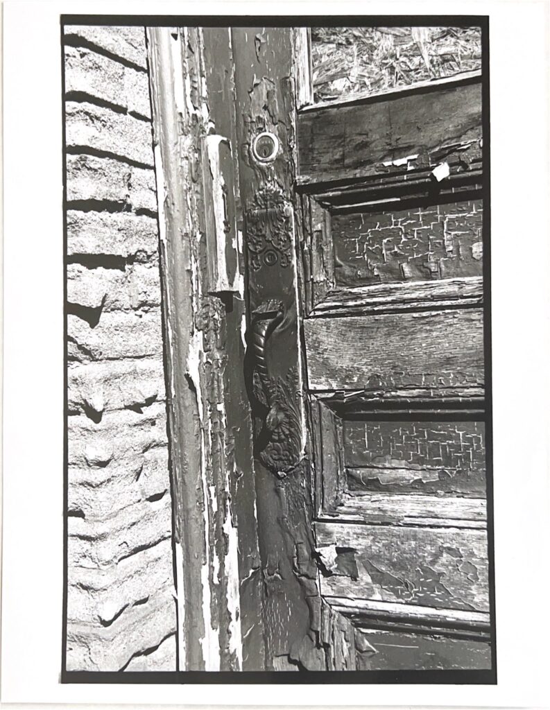 black and white photo of old wood door with significant wear and textural contrast of stone wall on left