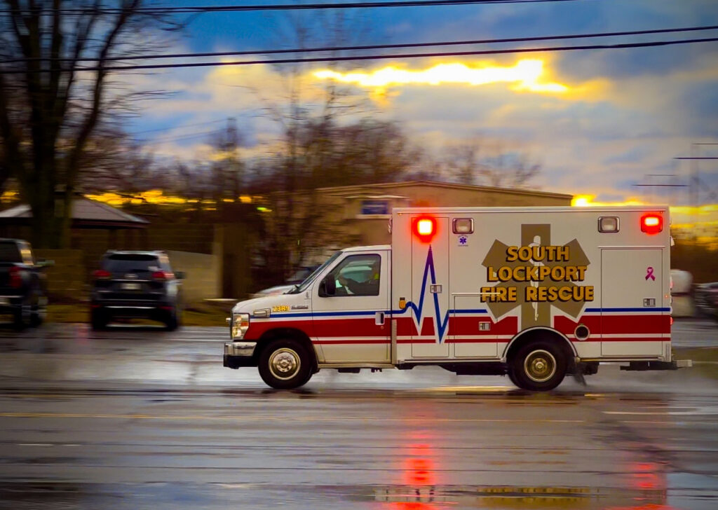 Ambulance in action, lights flashing, wet road