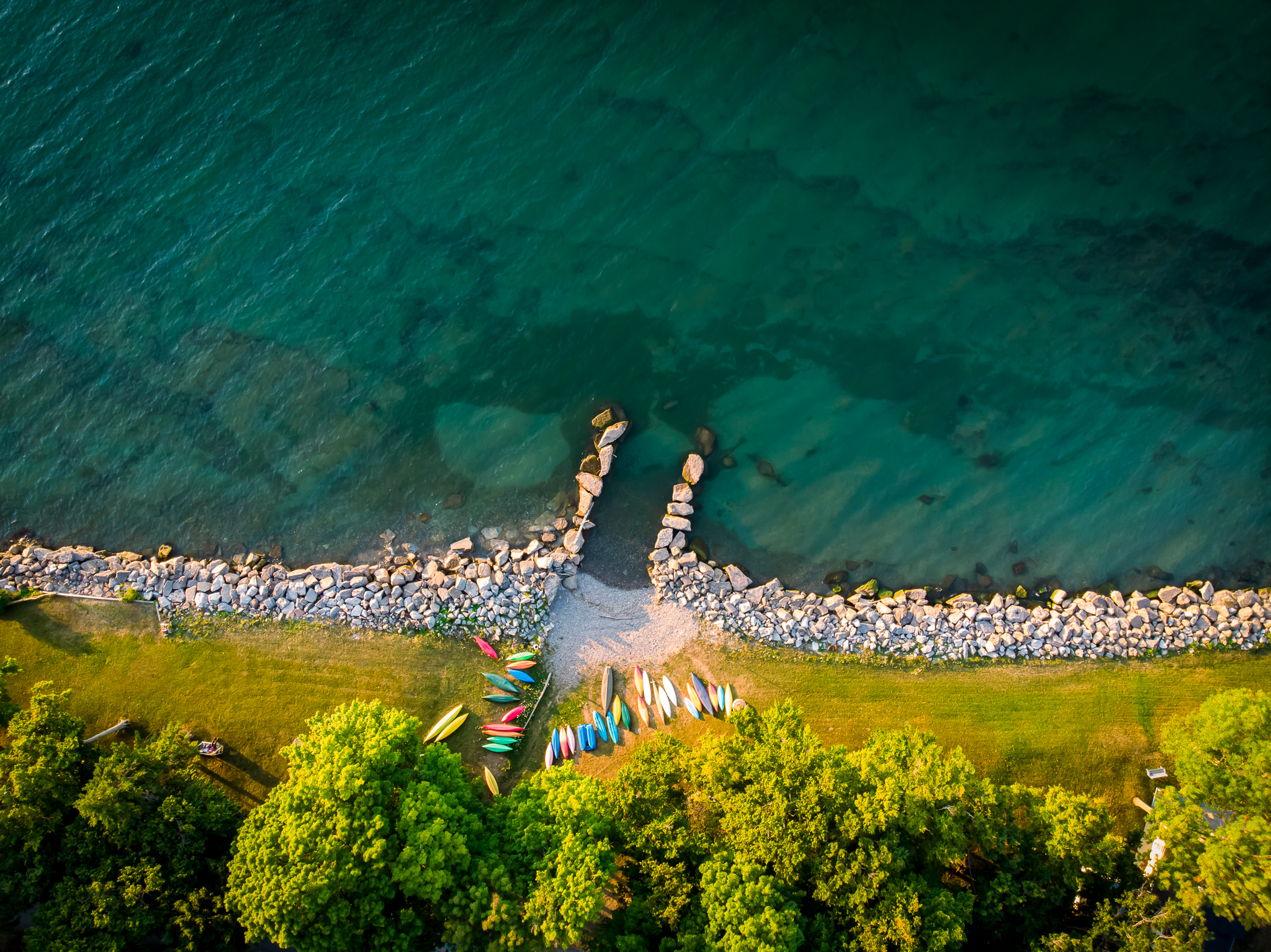 aerial image of lakeshore with rocks along shorelines, colorful canoes, and bright blue-green water