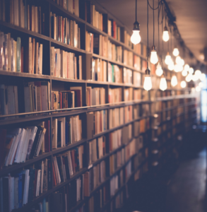late nights at the library image of dark bookshelf with hanging lights