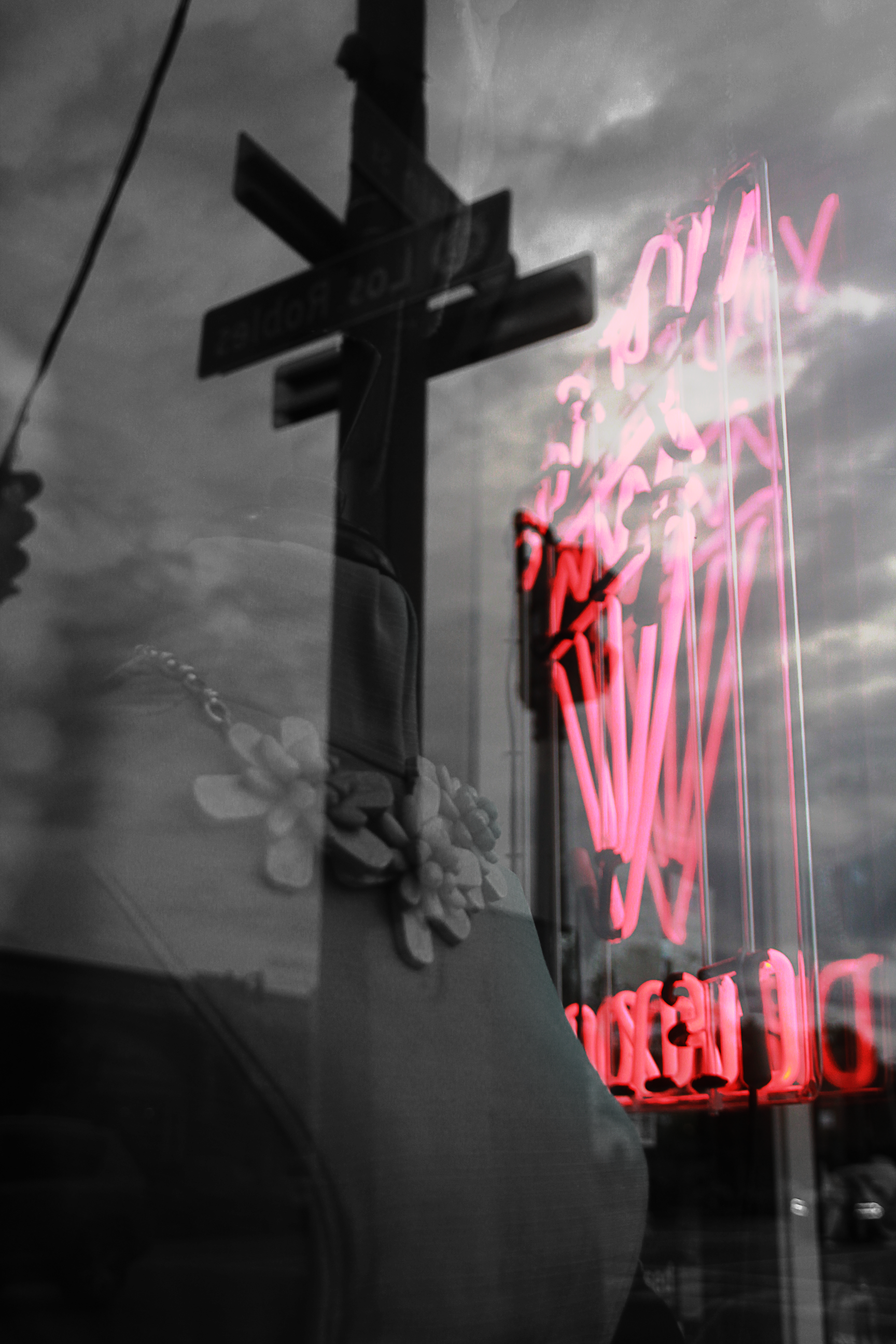 image of shop window displaying bust with necklace, and reflection of street signs and neon sign 
