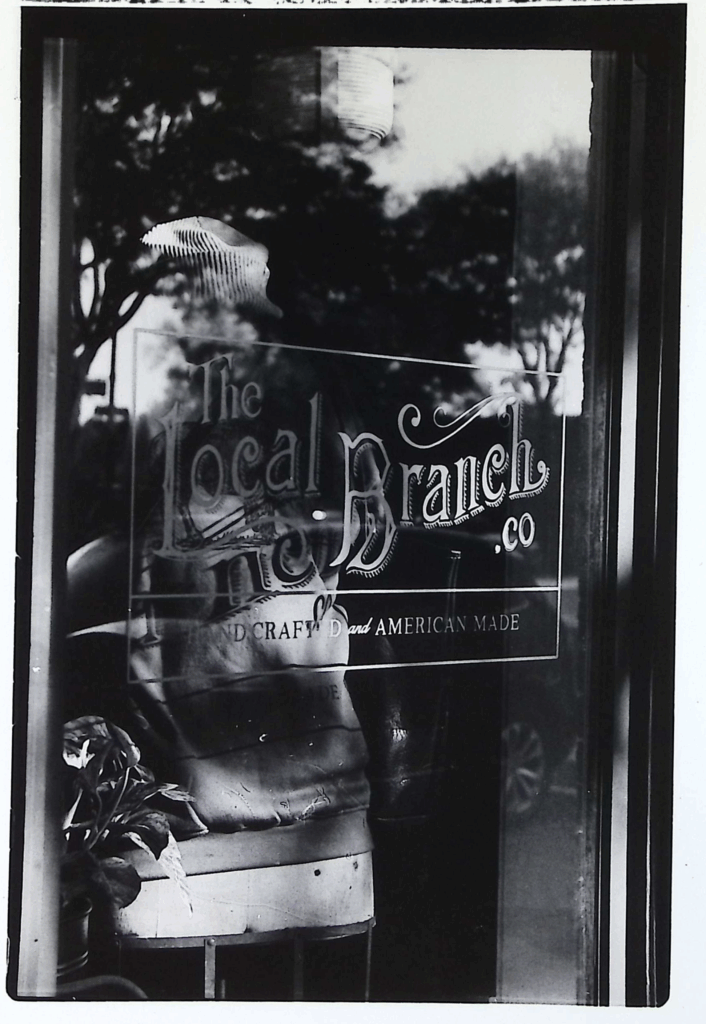Black and white image of storefront glass with signage "The Local Branch"
