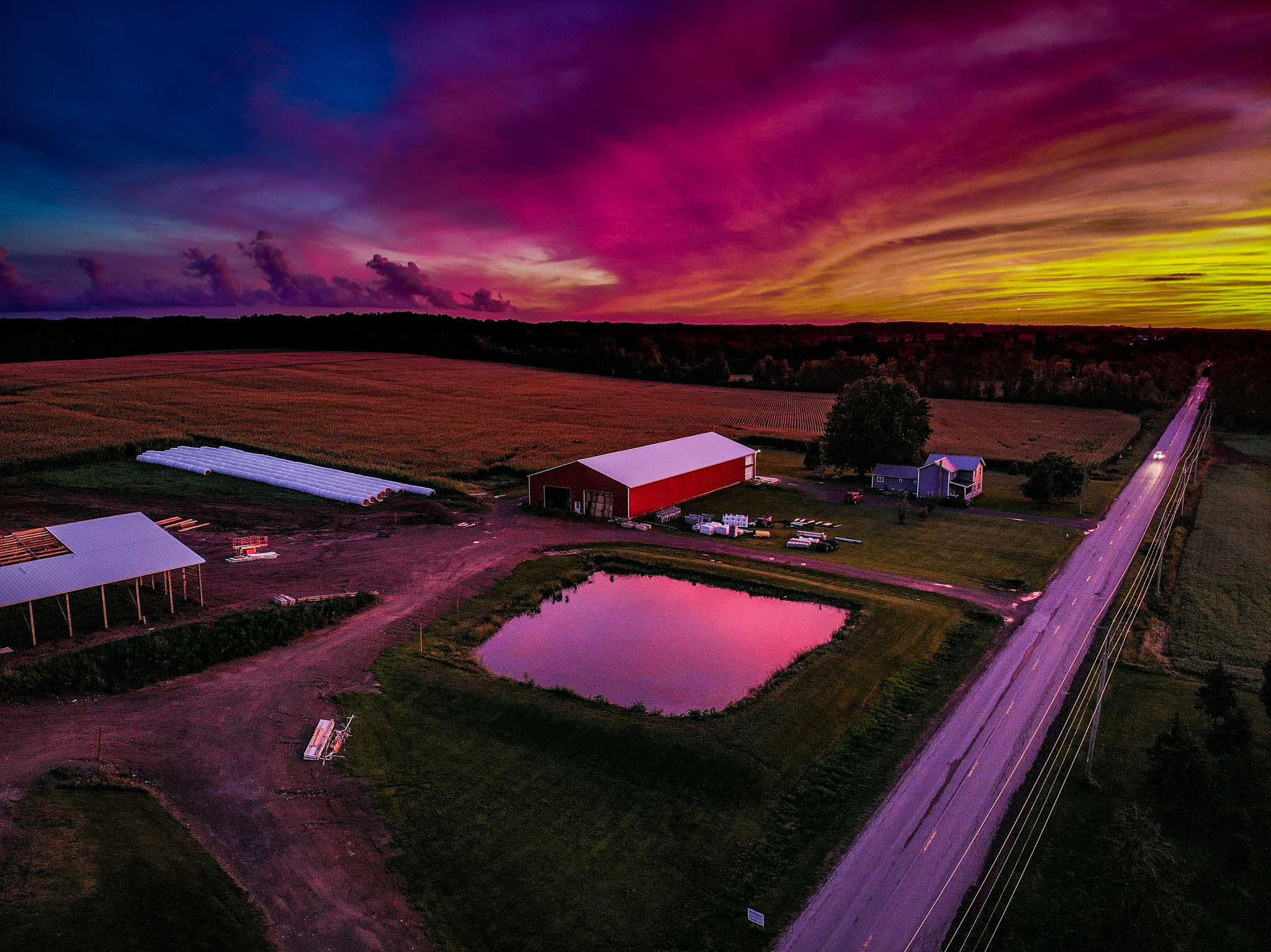 aerial photo of farm with pond at center and colorful sunset