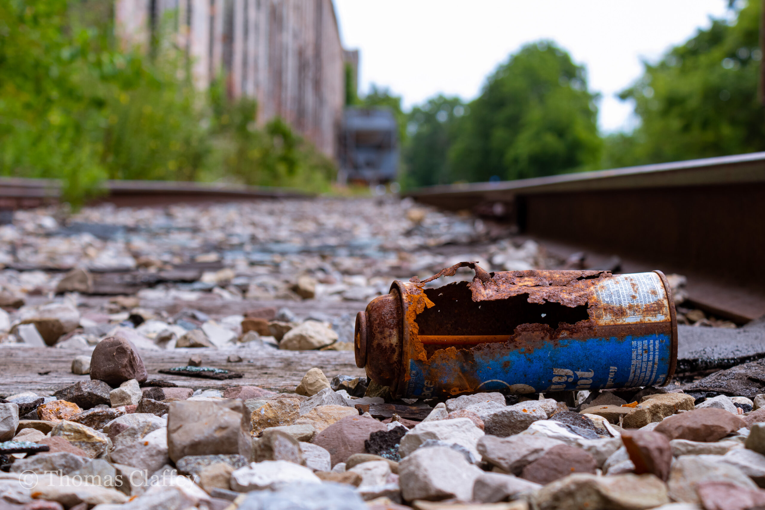rusty paint can in foreground, train tracks and rocks in background