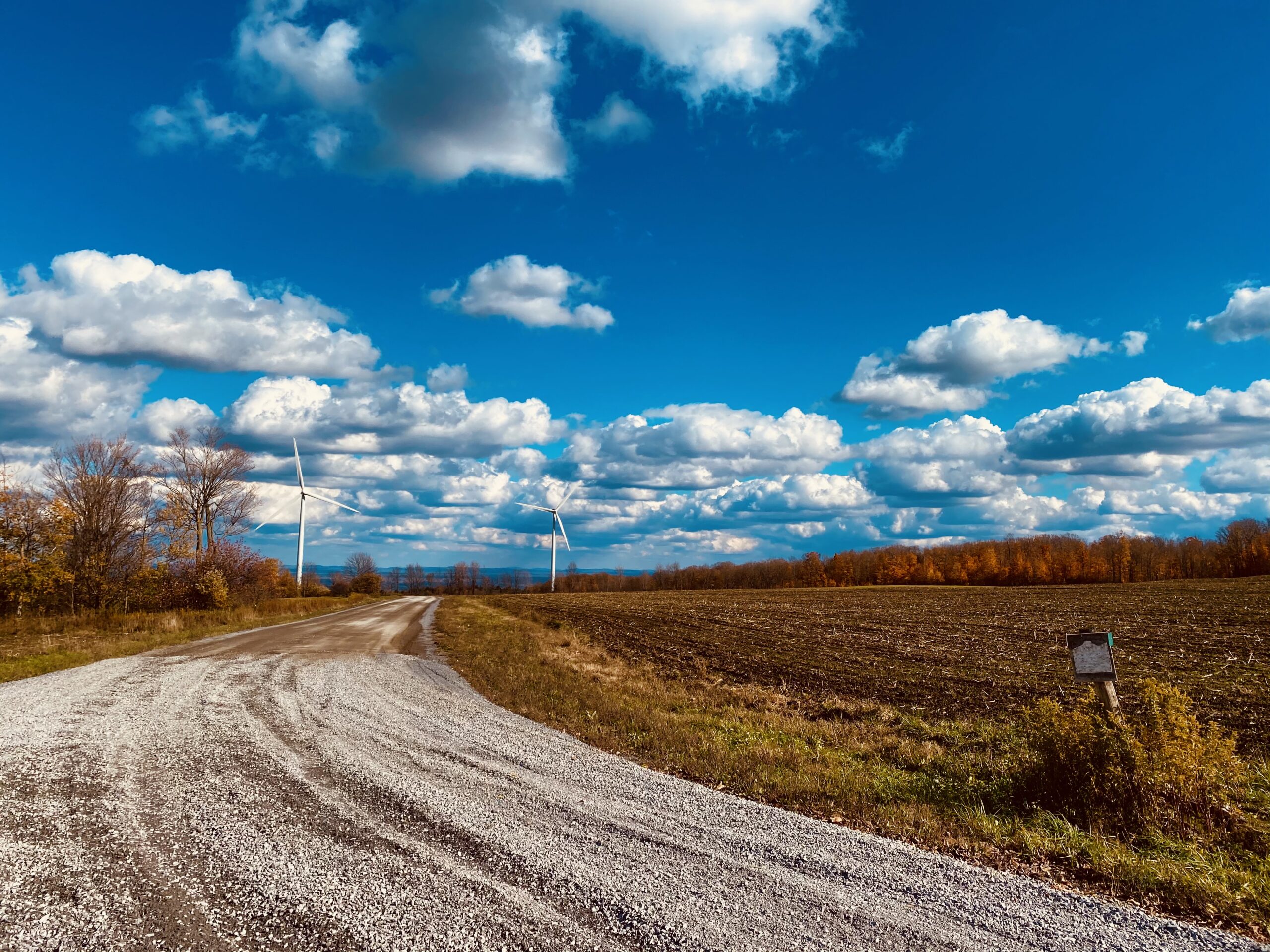 photo of dirt road with windmills and blue sky/clouds in background